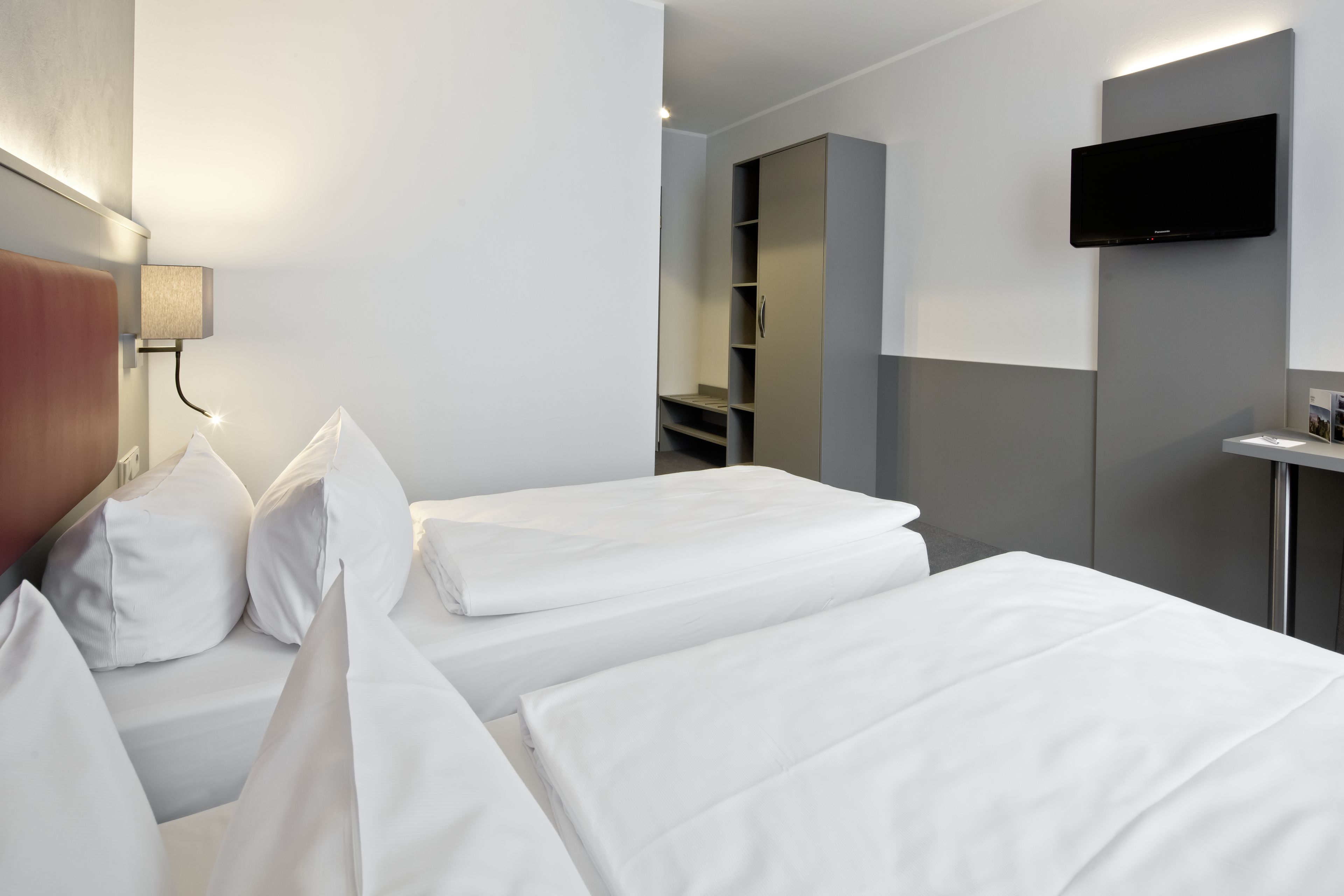 A hotel room with two beds, a TV mounted on the wall, and a wardrobe.