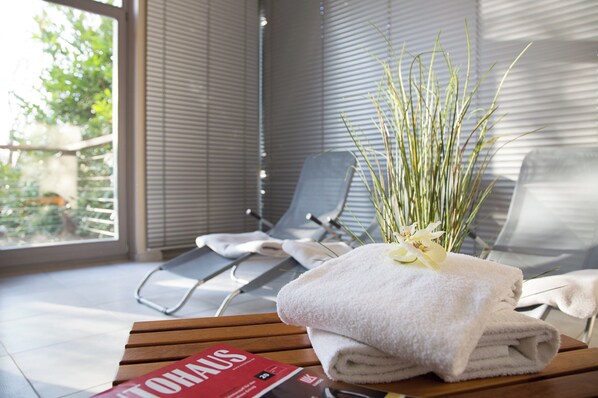 Una habitación con ventana, una silla, una toalla y una revista sobre una mesa.