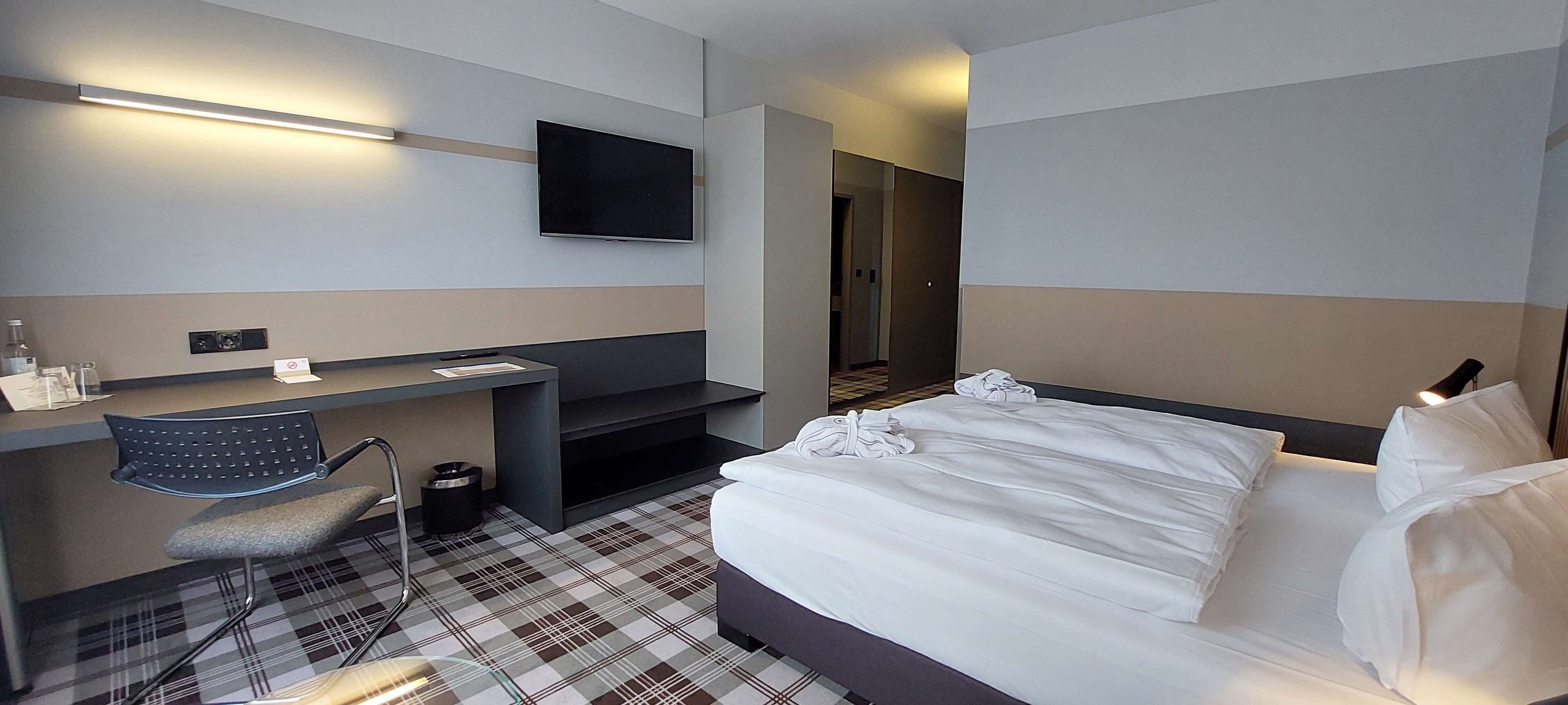 A hotel room with a bed, a desk, a chair, a television, and a check-in counter.