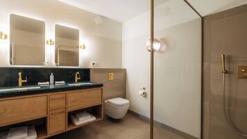 Une salle de bain moderne avec une douche à l’italienne en verre, un meuble-lavabo en bois avec un plan de travail foncé et des toilettes blanches.