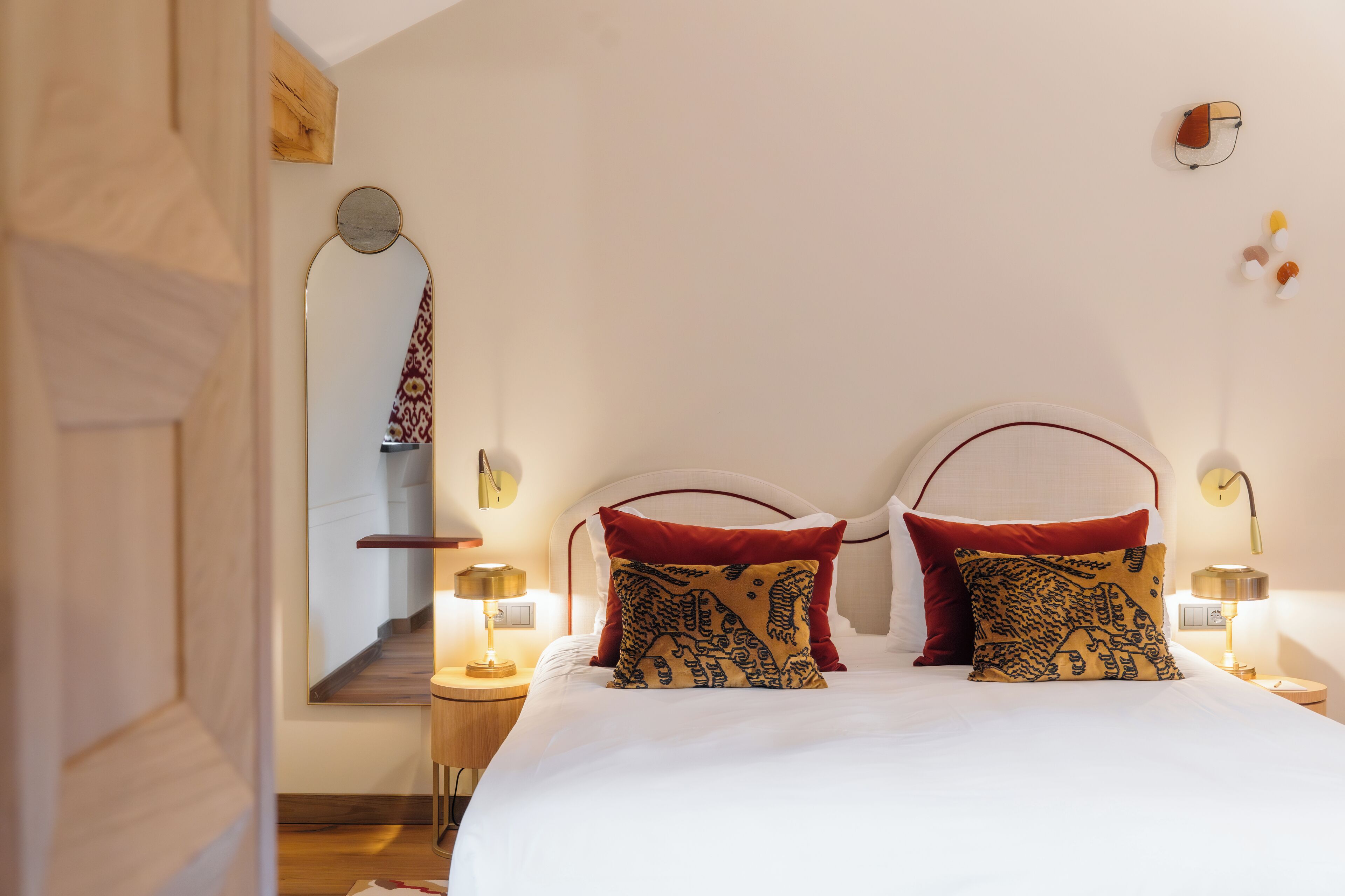 Un lit bien fait, avec deux oreillers, une table de chevet avec une lampe et un miroir au mur.