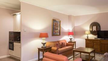 A living room with a sofa, two side tables with lamps, a television, and a kitchen area with cabinets and a microwave.