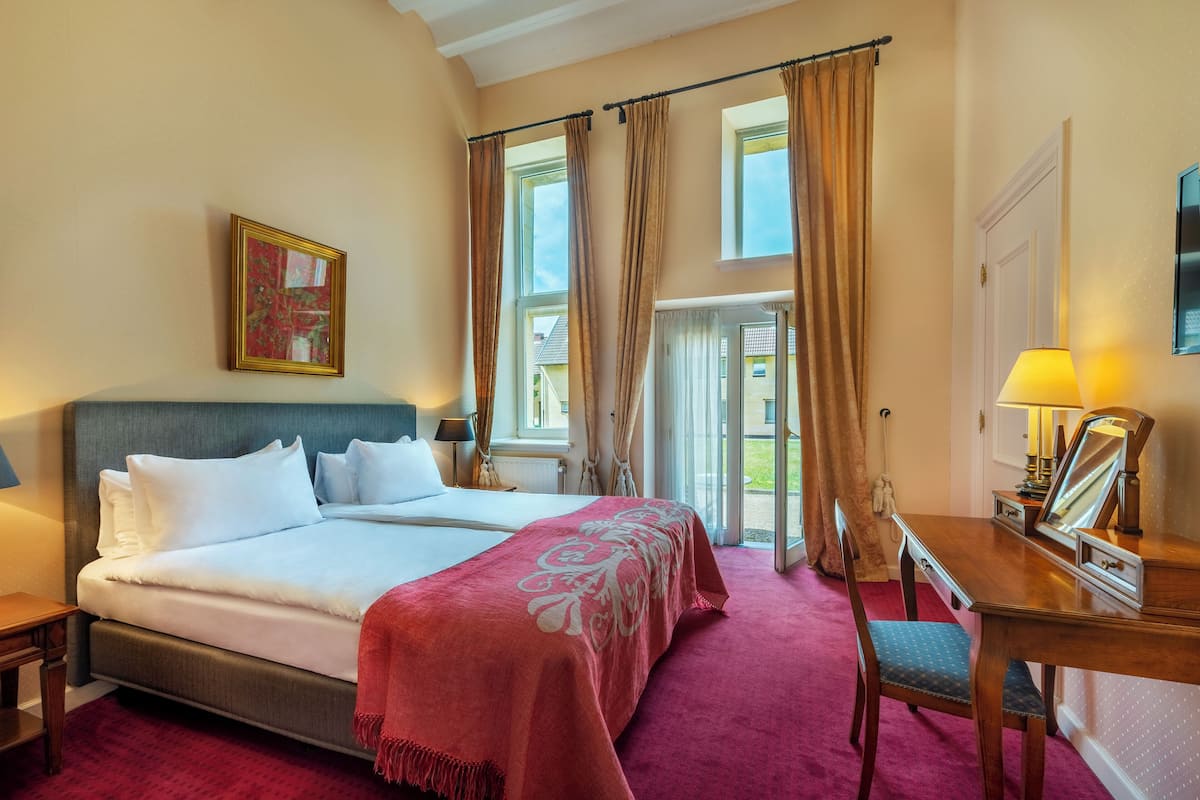 Une chambre d’hôtel avec un grand lit, un bureau avec un miroir et une vue sur l’extérieur par les fenêtres.