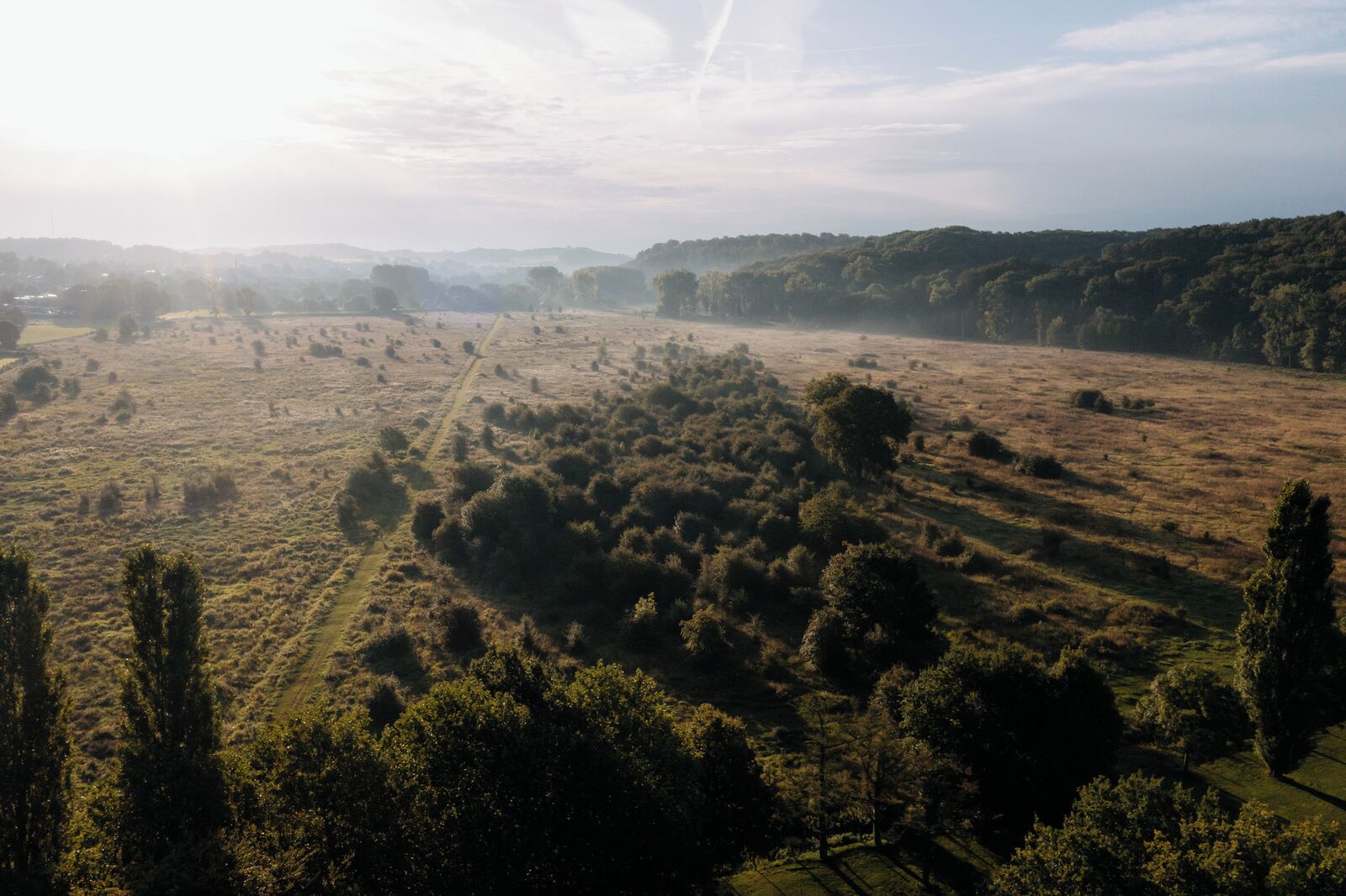 Luchtbeeld van een landelijk gebied met velden, bomen en een heldere lucht.