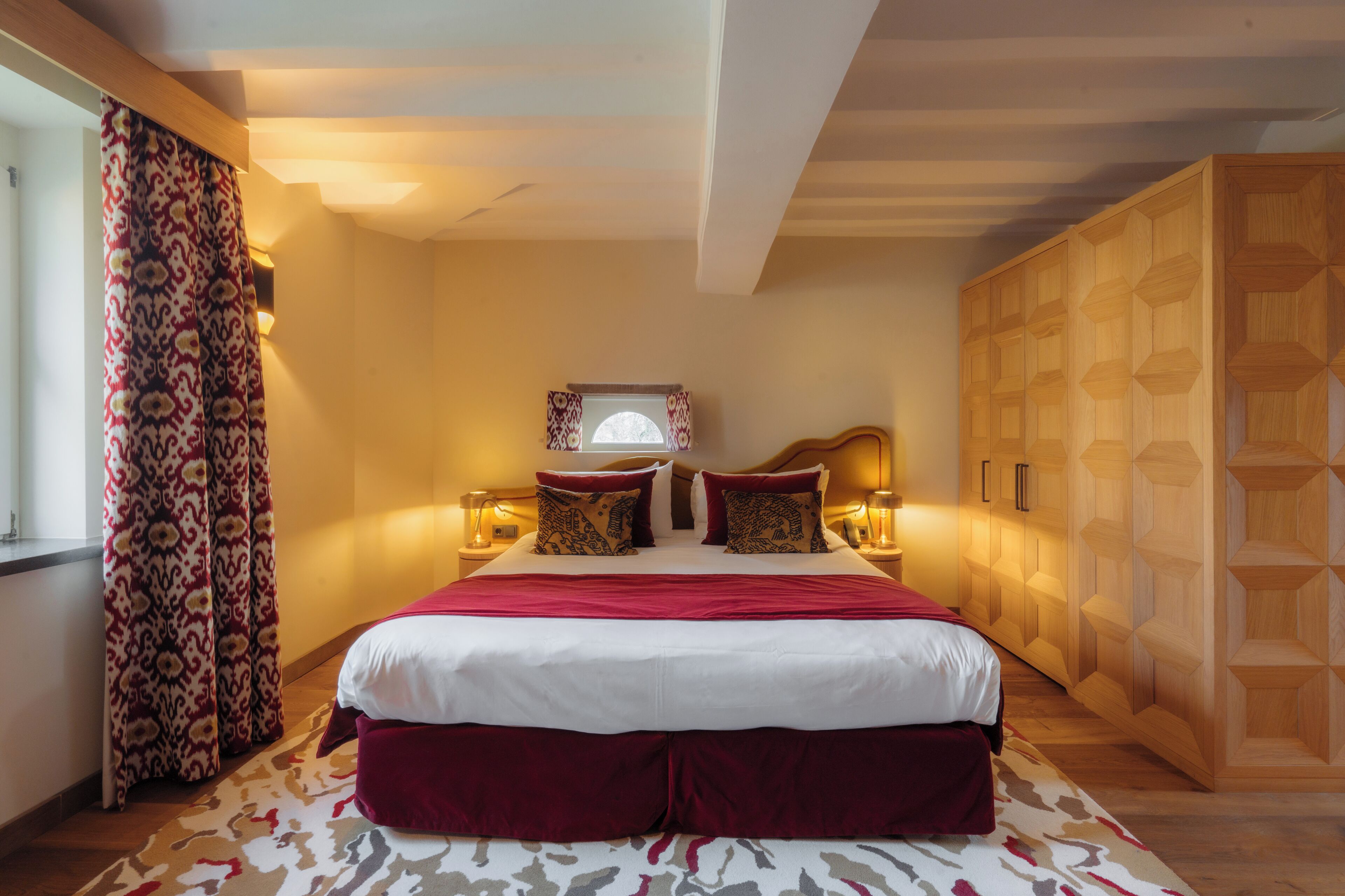 A bedroom with a large bed, patterned curtains, a wooden wardrobe, and bedside lamps.