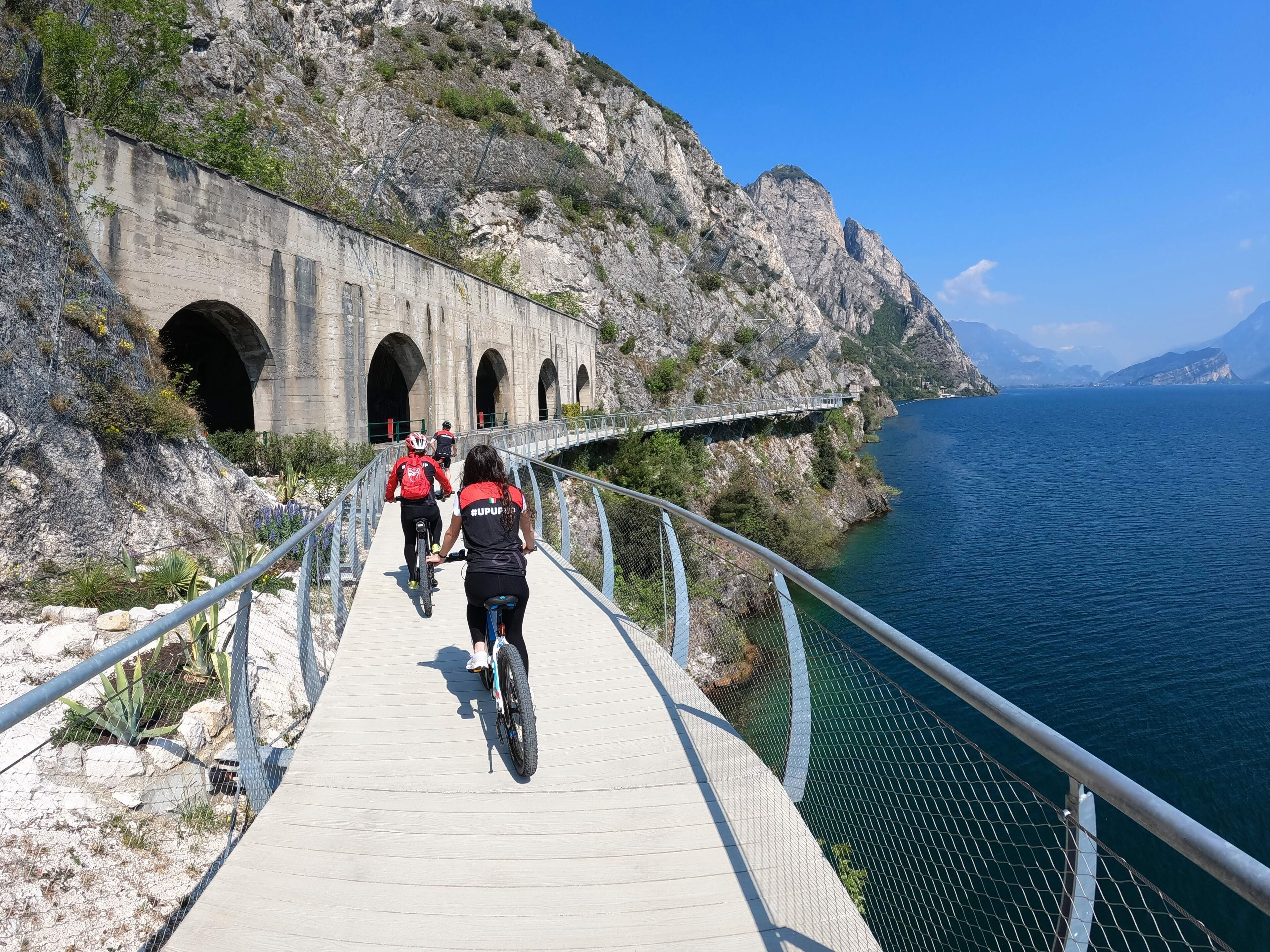 Een pad met fietsers, een brug en een rotsachtige klif boven een wateroppervlak.