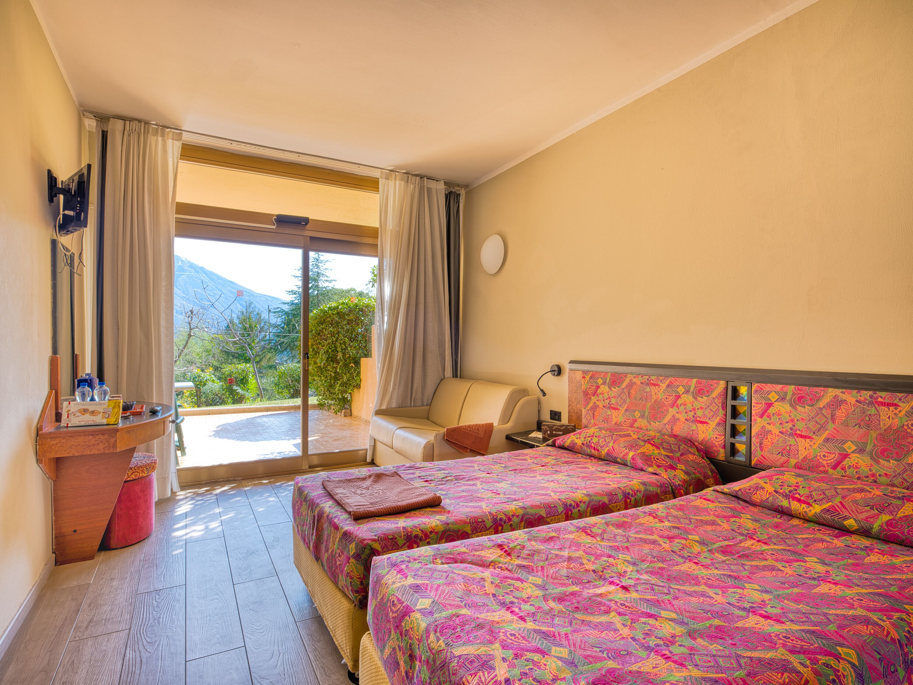 A hotel room with two beds, a small table, a chair, and a view of the outdoors.