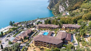 Vista aérea de un hotel costero con varias construcciones, una piscina y un camino que lleva a la playa.