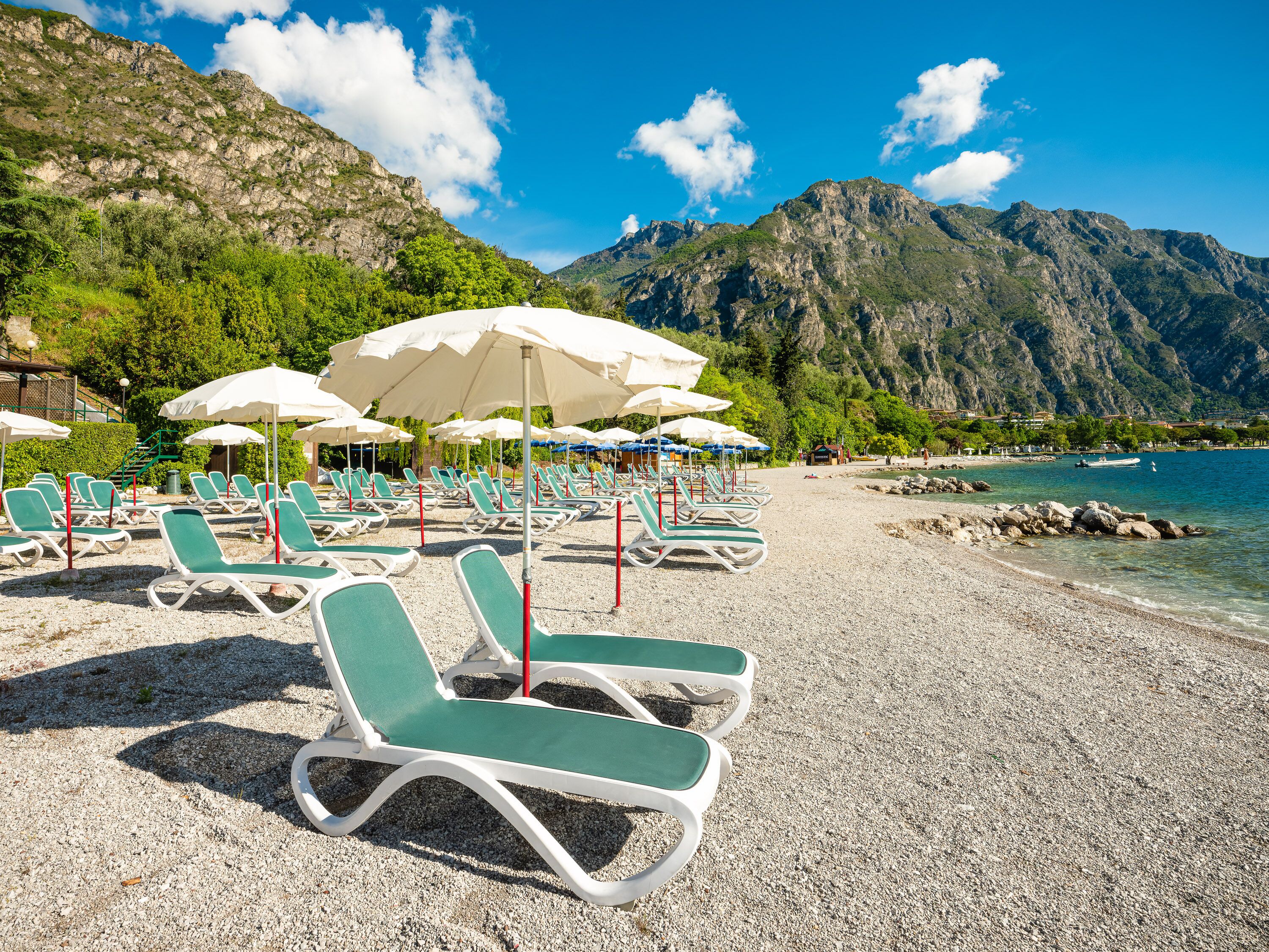 A beach with rows of sun loungers and umbrellas, a rocky shoreline, and mountains in the background.