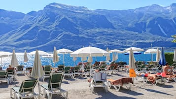 A beach with rows of sun loungers and umbrellas, a clear view of the sea, and mountains in the background.