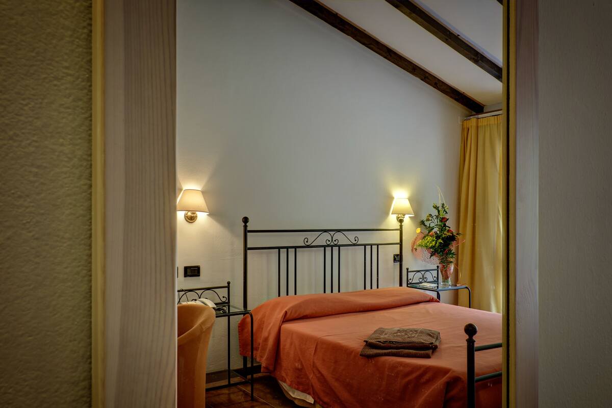 A bedroom with a bed, bedside lamps, a chair, and a nightstand with a plant.