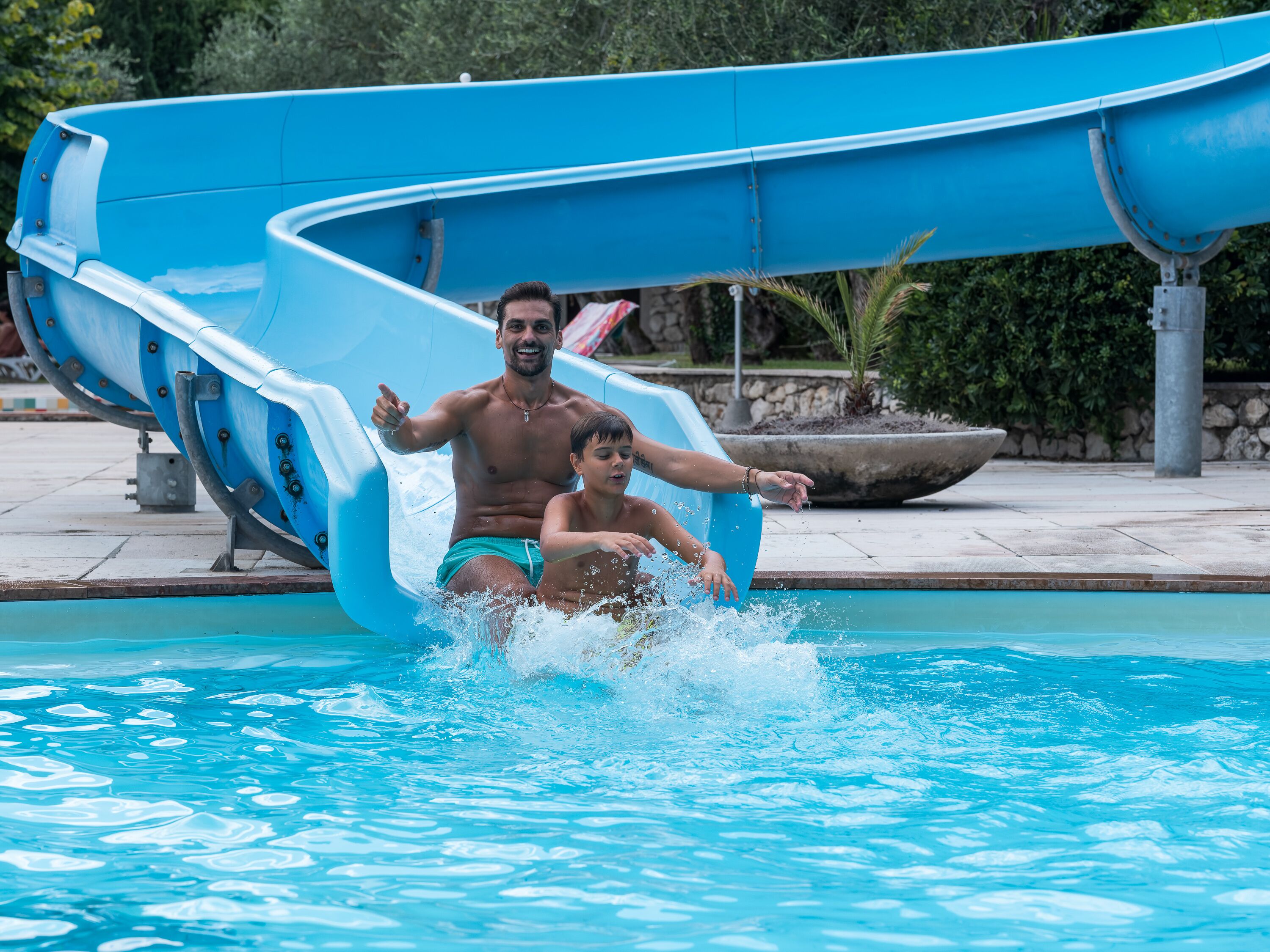 A water slide at a swimming pool with a man and a child at the bottom.