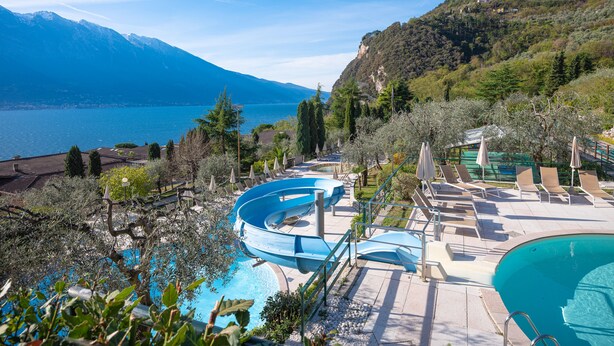 Un resort con piscina, sillas de descanso y vistas a un lago y montañas.