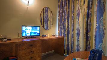 A hotel room with a wooden desk, a television, a telephone, a mirror, and patterned curtains.