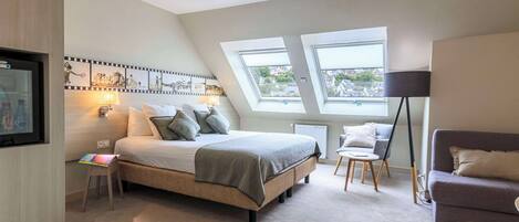 A modern bedroom with a large bed, skylights, a desk, and a sofa.