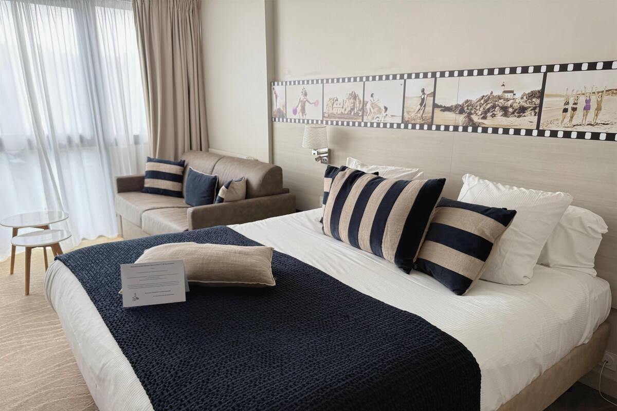 Habitación de hotel con una cama grande, un sofá, una mesita y un cuadro mural con motivos de fotogramas de película.