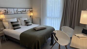 Un cuarto de hotel ordenado con cama, una silla, un escritorio y una lámpara.