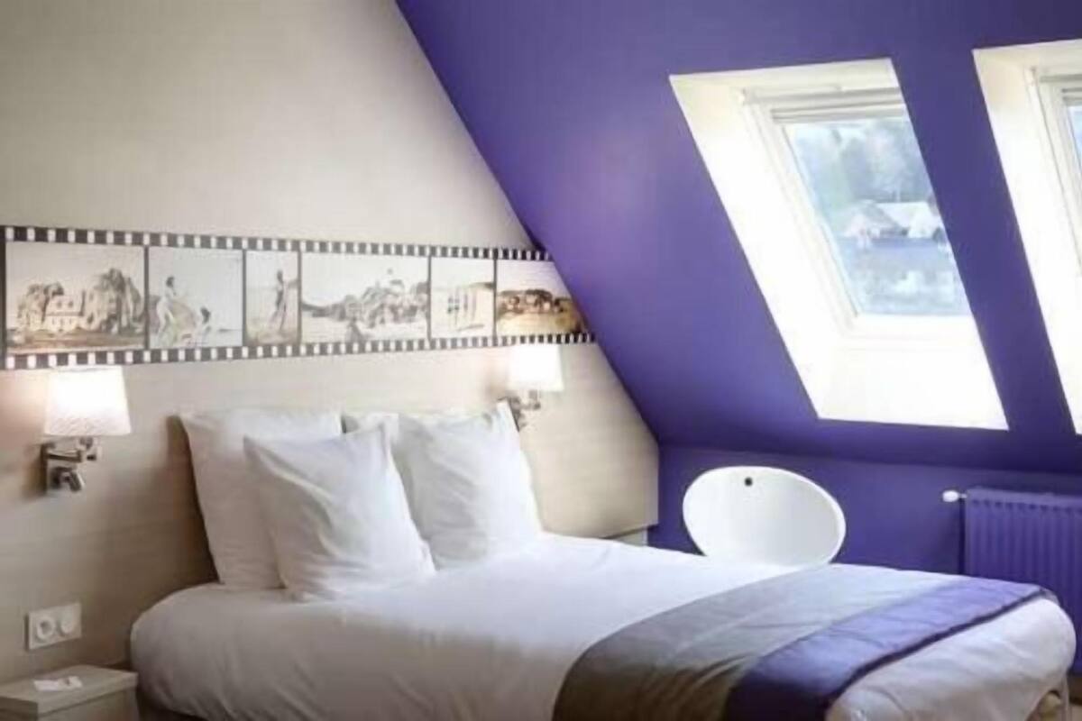 Un dormitorio con cama, mesita de noche, lámpara, silla y tragaluz.