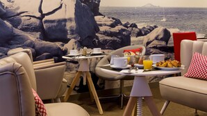 A dining area with a table set for breakfast, overlooking a rocky coastline with a lighthouse in the distance. - Best Western Les Bains Hôtel & SPA Perros-Guirec (Perros-Guirec)