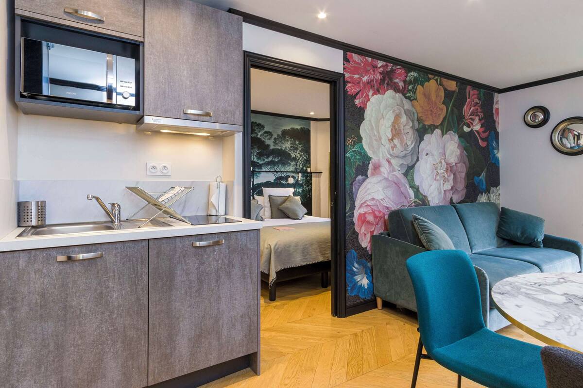 Una cocina moderna con microondas integrado, un lavamanos y una encimera. Hay un comedor con una silla azul y una mesa redonda.