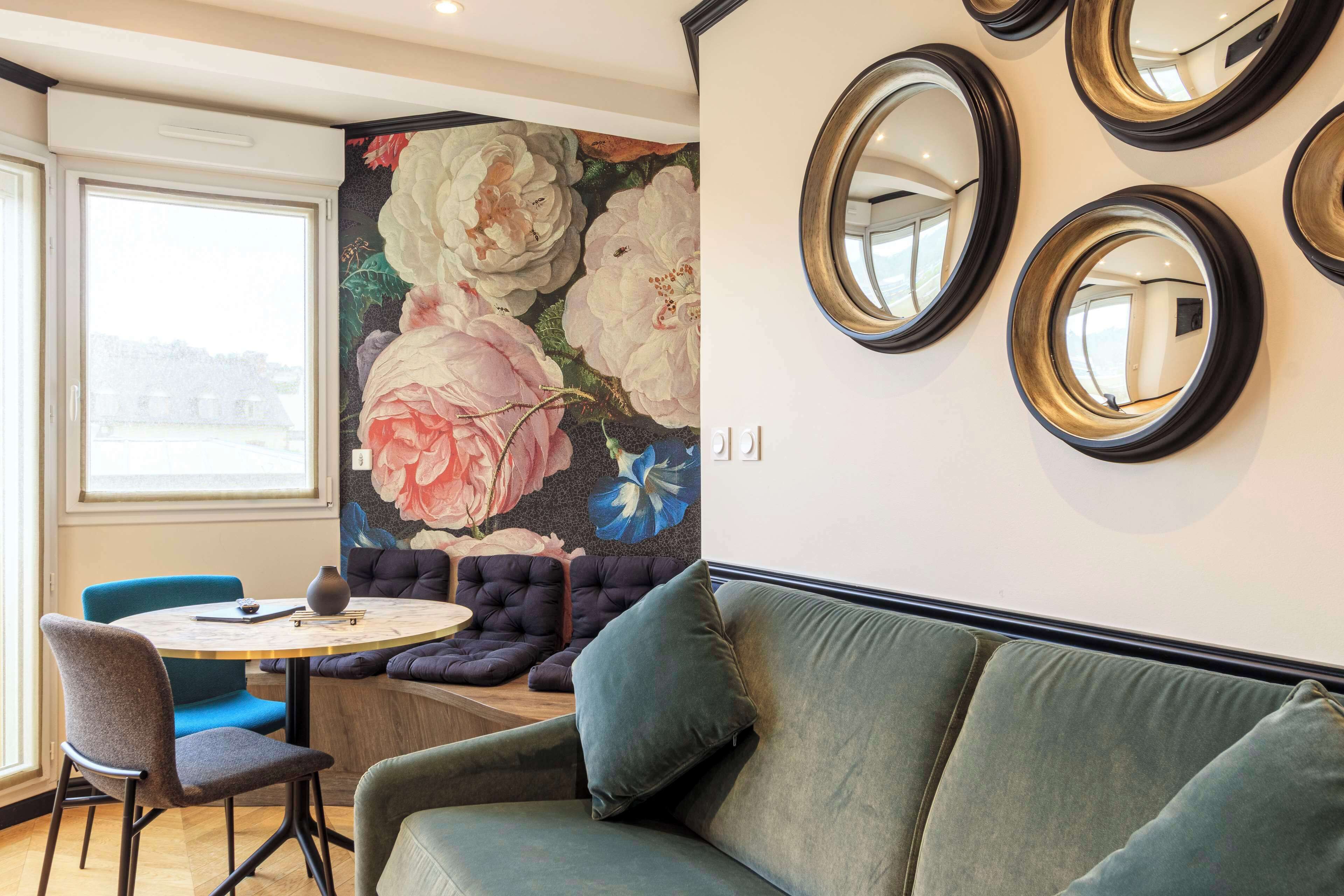 Ein Zimmer mit einem runden Tisch, blauen Stühlen, einem grünen Sofa und einer Wand mit floralem Wandbild.