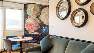 A room with a round table, blue chairs, a green sofa, and a floral mural on the wall.