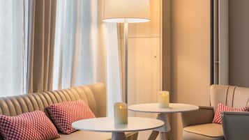 A modern hotel room with a sofa, two small round tables, and a floor lamp.