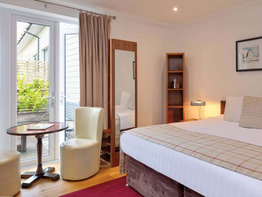 A hotel room with a bed, a chair, a small table, a bookshelf, and a window with curtains.