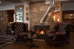 A cozy lounge area with leather armchairs, a small table with glasses, a fireplace, and stone walls.