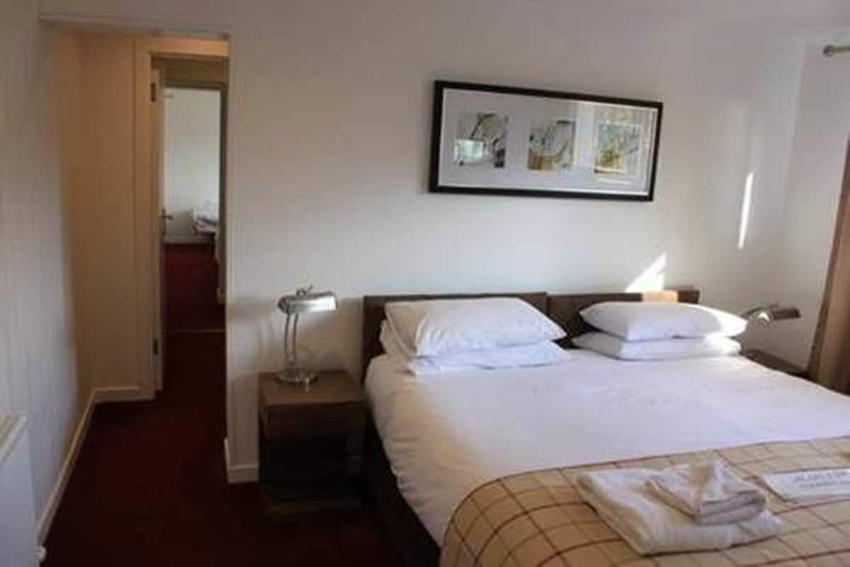 A hotel room with a bed, a nightstand, a lamp, and a framed picture on the wall.