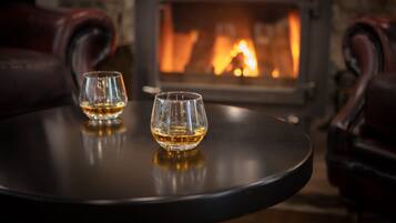 Two glasses of whiskey on a round table with a fireplace in the background.