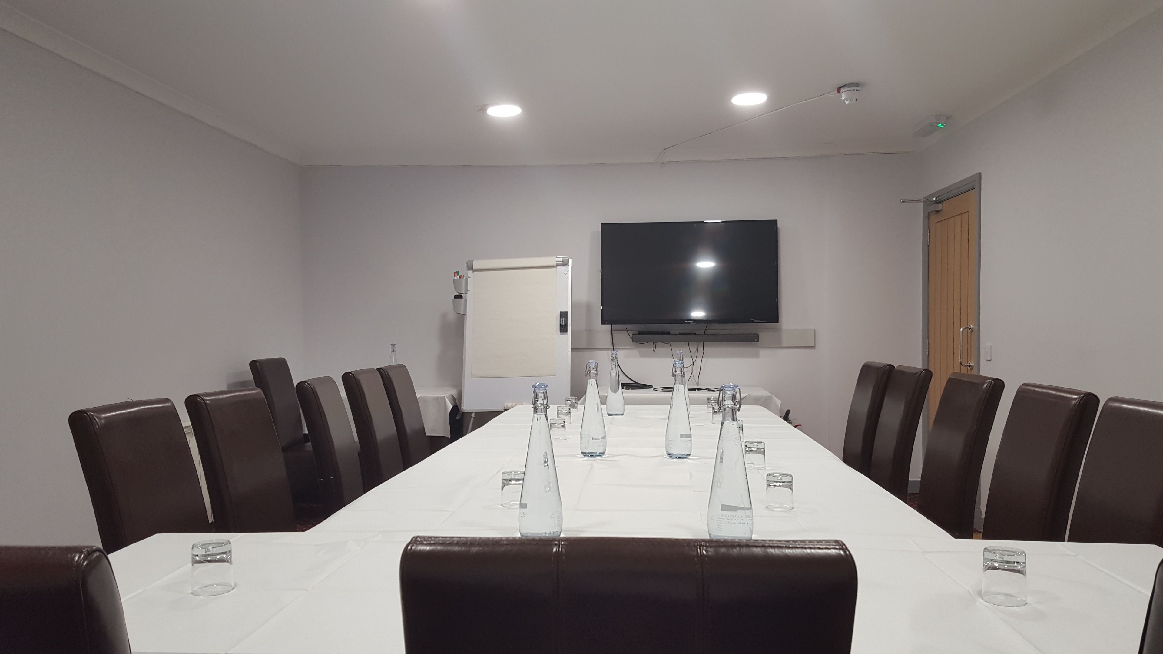 Un salón de conferencias con una larga mesa, sillas, un televisor y una puerta.
