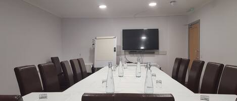 Un salón de conferencias con una larga mesa, sillas, un televisor y una puerta.