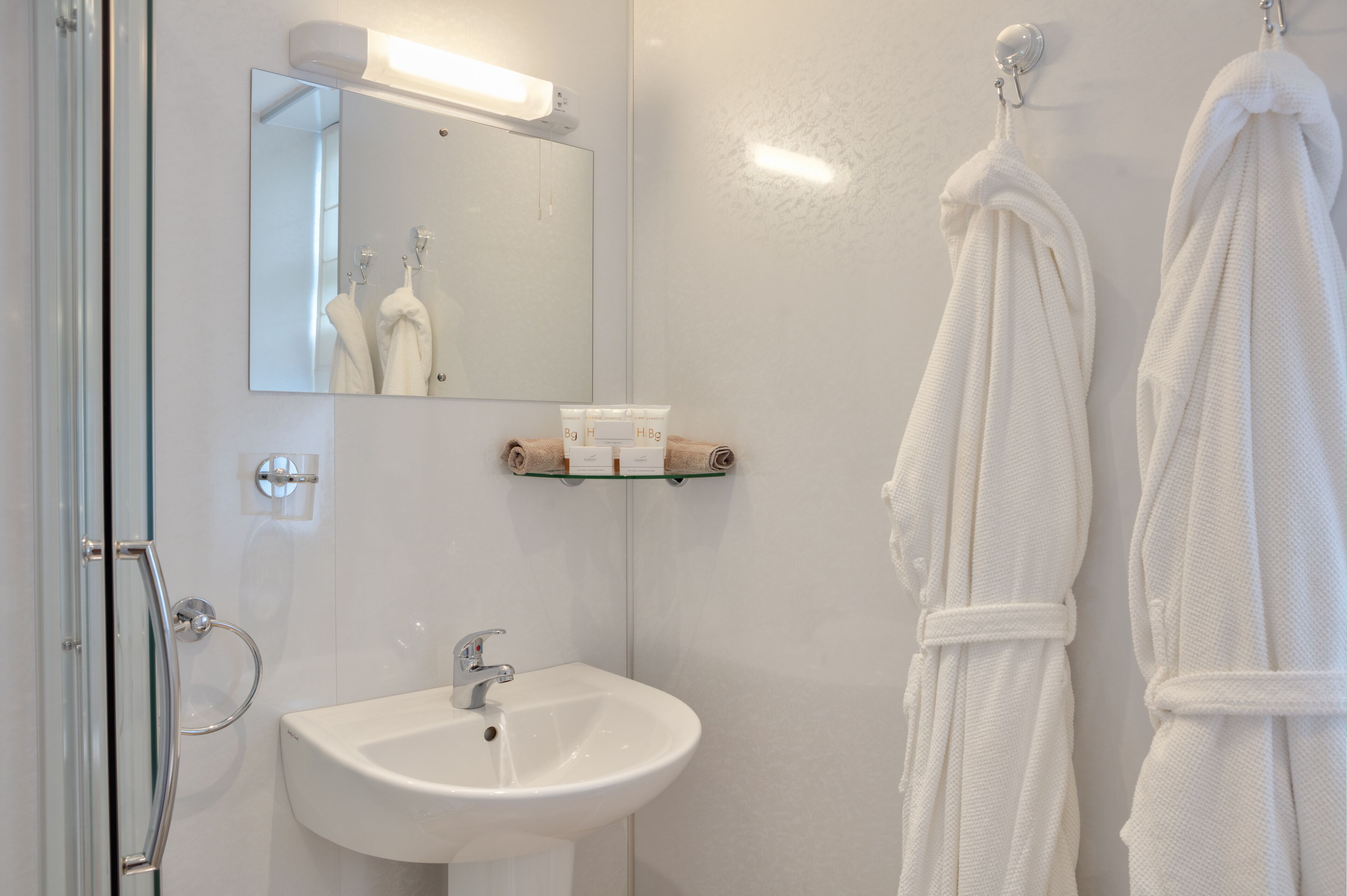 A bathroom with a glass shower door, a white sink, a mirror, and two white towels hanging on hooks.
