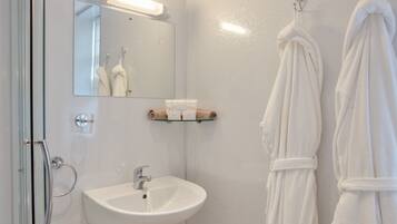 A bathroom with a glass shower door, a white sink, a mirror, and two white towels hanging on hooks.
