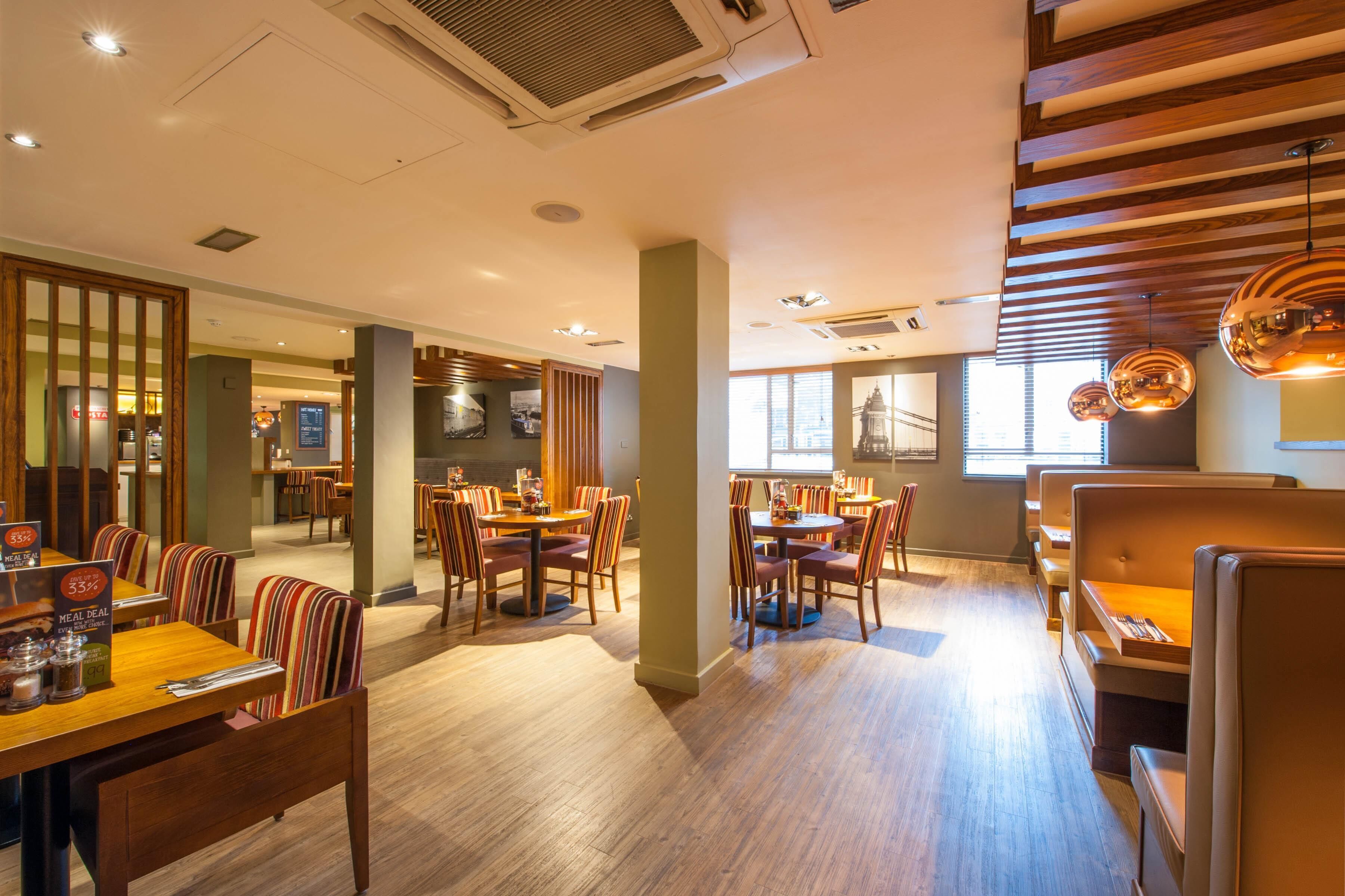 A restaurant with wooden flooring, striped ceiling, and multiple dining tables with chairs.