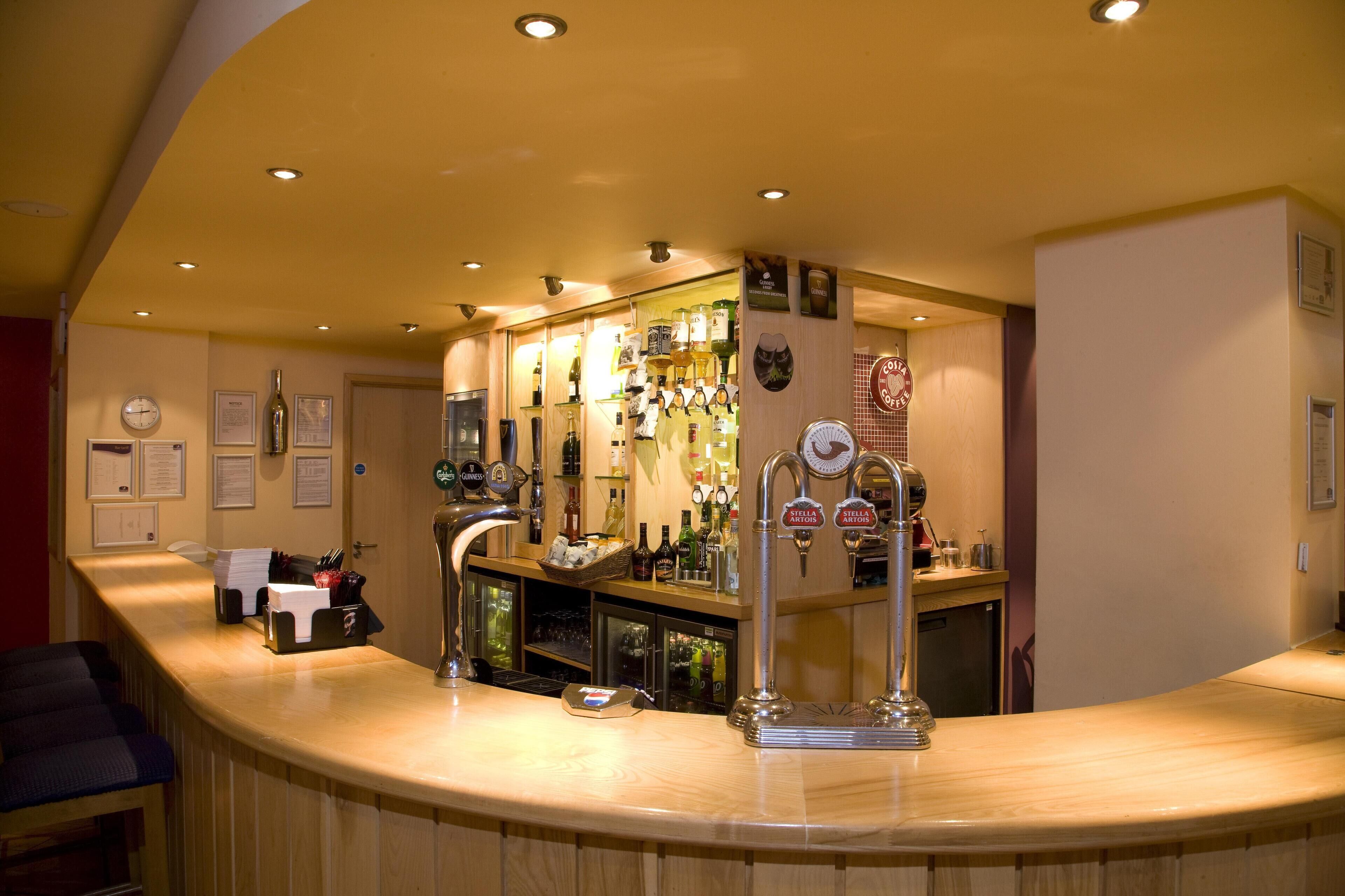 A bar area with a counter, bar stools, and a variety of bottles and glasses.