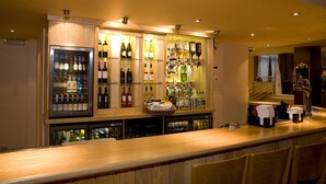 Zona de bar amb un taulell de fusta, ampolles de vi i un frigorífic.