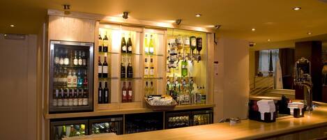 Un espace bar avec un comptoir en bois, des bouteilles de vin et un réfrigérateur.