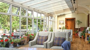A conservatory with large windows, a wooden table, and several armchairs with plaid cushions. - Renvyle House Hotel & Resort (Renvyle)