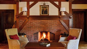 A cozy room with a brick fireplace, two armchairs, and a table with a book. - Renvyle House Hotel & Resort (Renvyle)