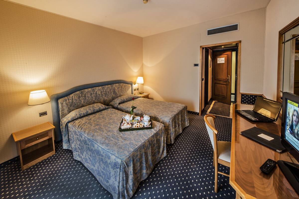 A hotel room with two beds, a desk with a laptop, and a TV.