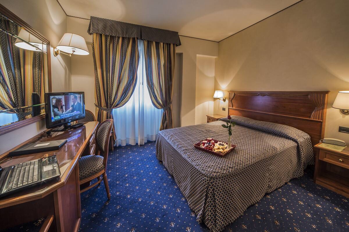 A hotel room with a bed, a desk with a computer, a television, and a telephone.