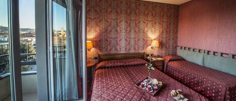 A hotel room with a large window, a bed with a quilted cover, two bedside tables with lamps, and a view of a cityscape.