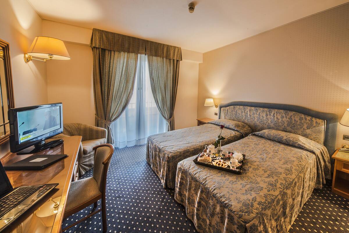 A hotel room with two beds, a desk with a computer, a chair, and a tray of breakfast items.