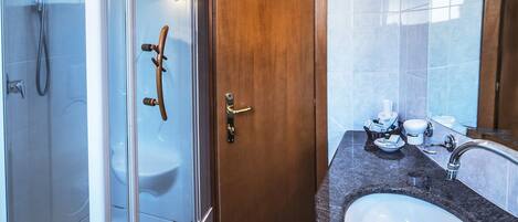 Un baño moderno con ducha de vidrio, puerta de madera, piso de mármol y encimera de granito con lavamanos y espejo.