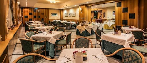 A hotel dining area with multiple tables and chairs, arranged in a spacious layout.