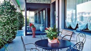 Un patio con una mesa redonda y sillas, plantas en macetas y vistas del interior del edificio.