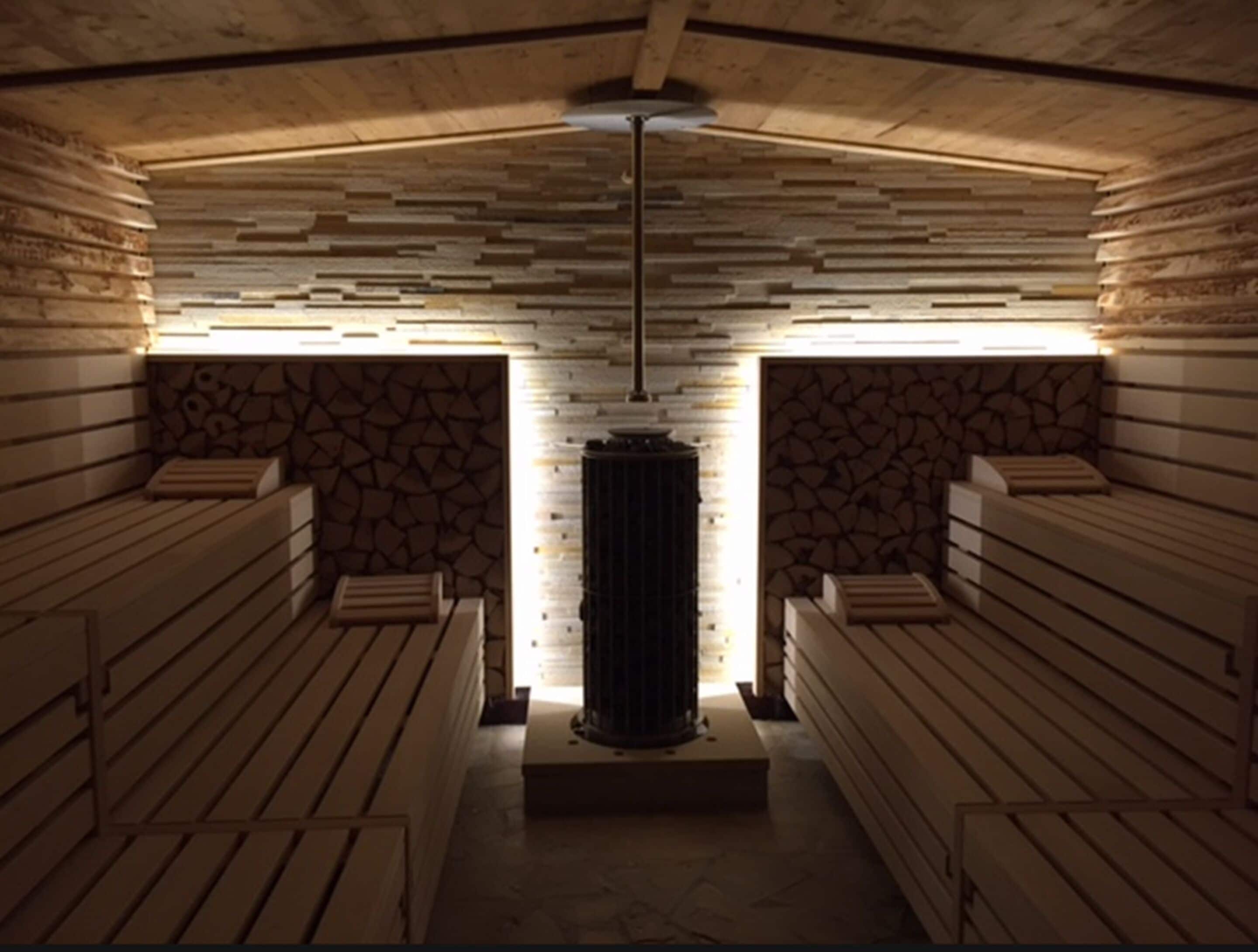 Eine Sauna mit Holzbänken, einer zentralen Säule und einer Wand im Steinmauerwerk.