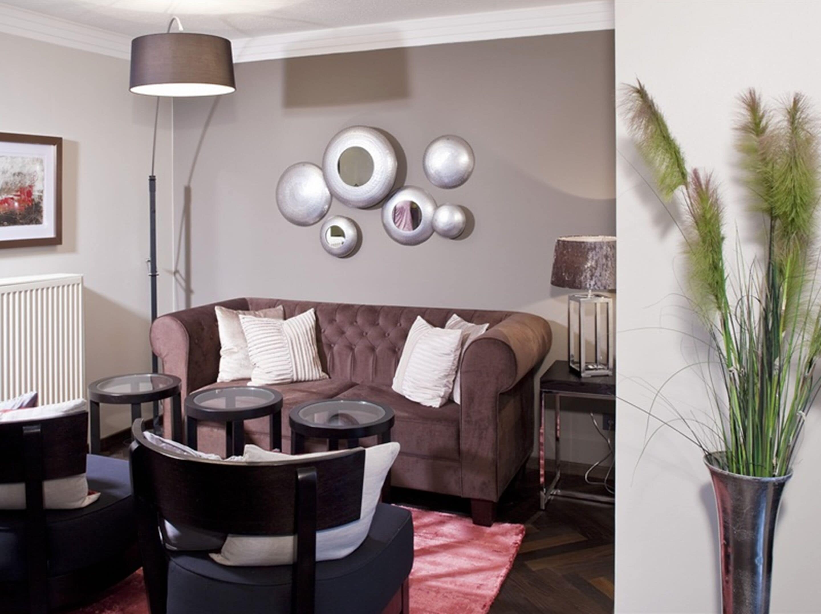 Un salon avec un canapé marron, trois miroirs ronds, une lampe, un vase avec des plantes vertes et un tableau encadré accroché au mur.